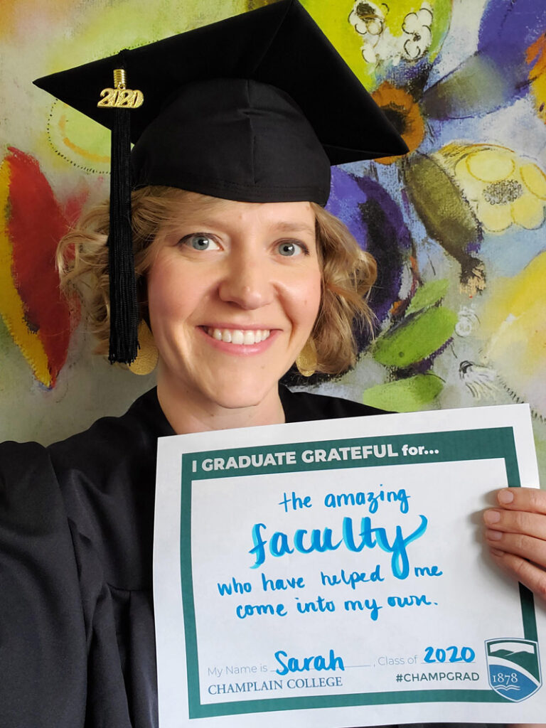 Graduate in full garb with a sign that says "I graduate grateful for the amazing faculty who have helped me come into my own."