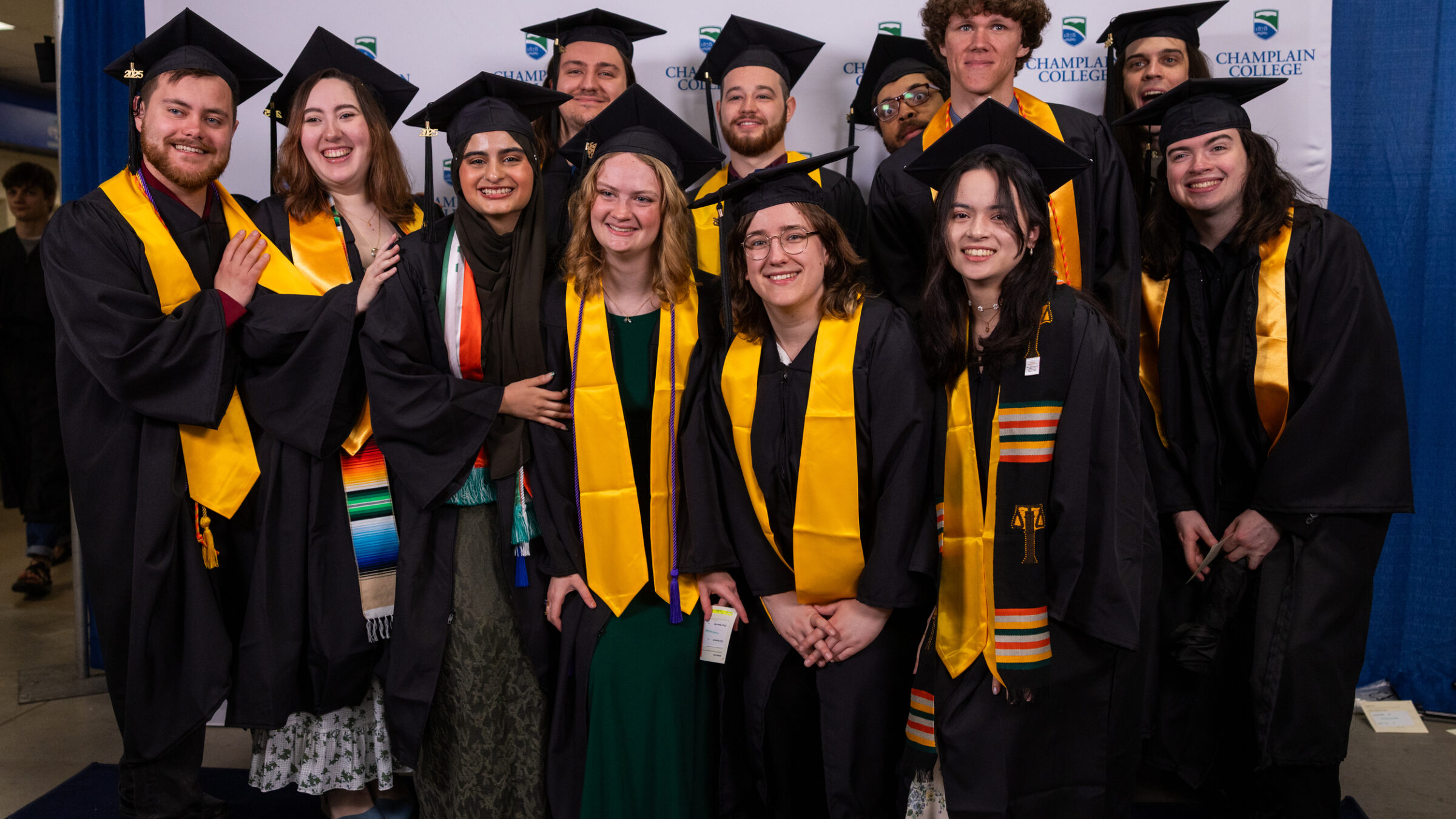 a group of 10+ graduates smile and pose for the camera together wearing their caps and gowns
