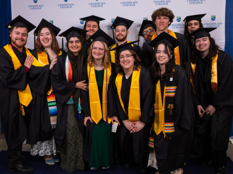 a group of 10+ graduates smile and pose for the camera together wearing their caps and gowns